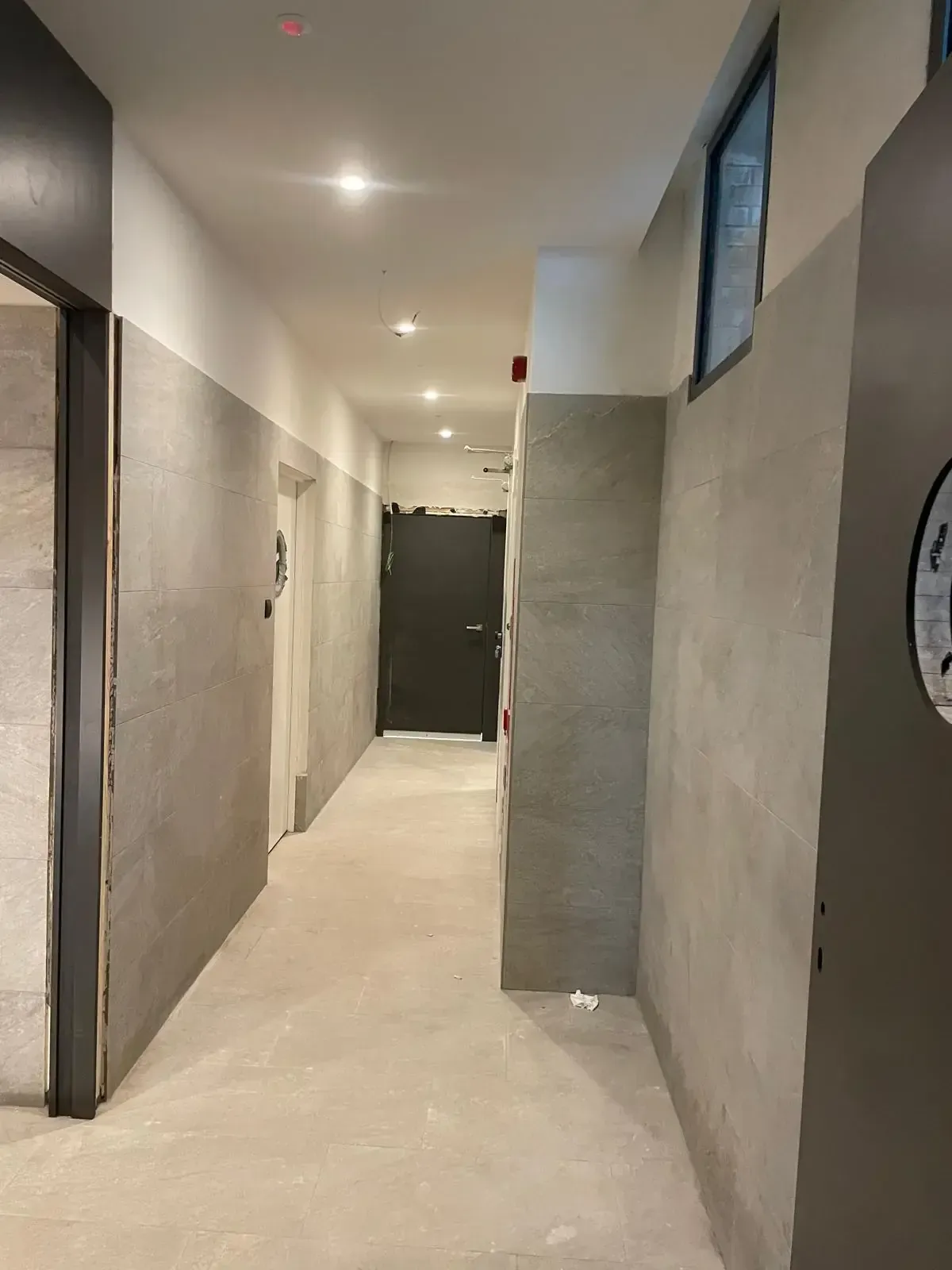 Pasillo largo con paredes grises, techo blanco y varias puertas cerradas.