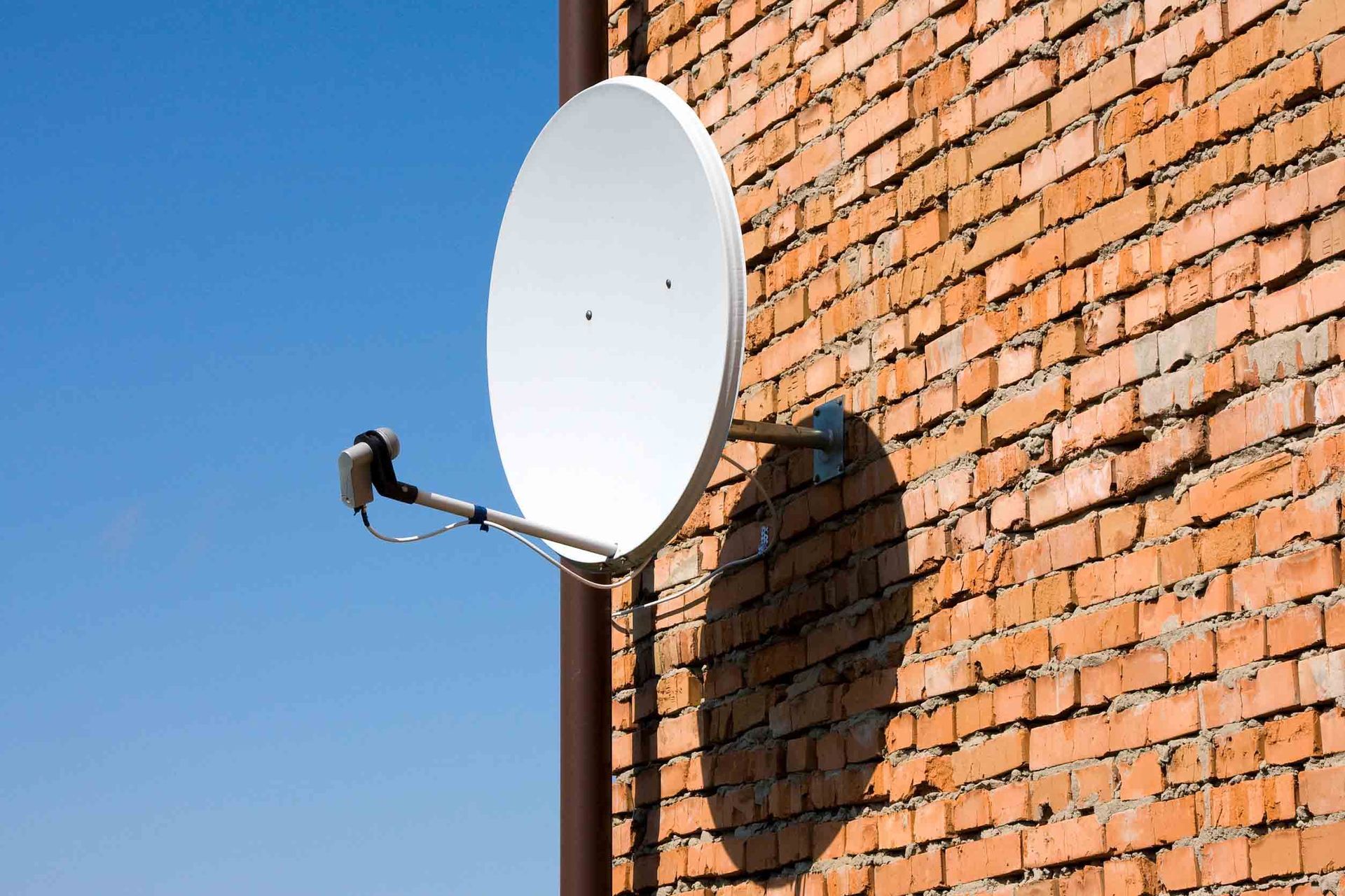 Una antena parabólica está montada en el lateral de un edificio de ladrillo.
