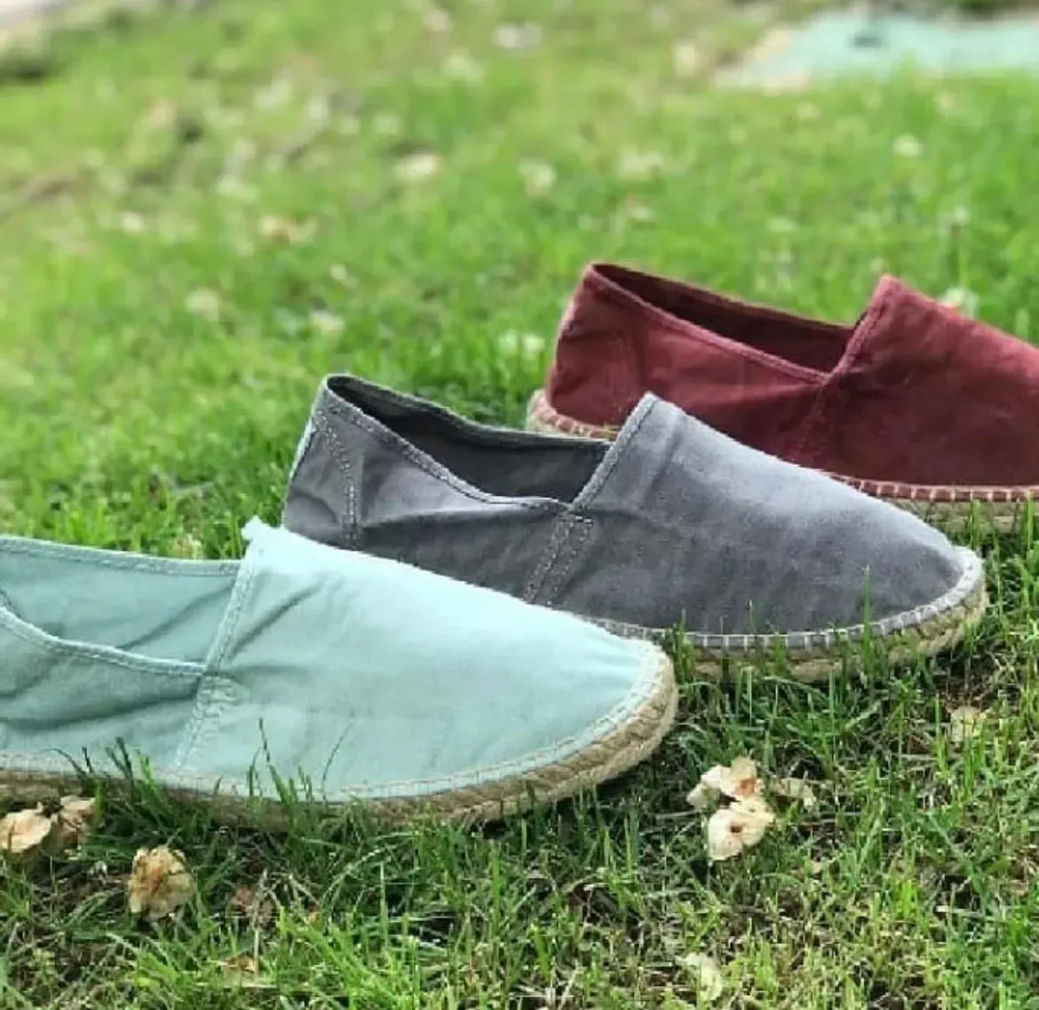 Tres alpargatas en color verde, gris y rojo sobre césped verde.