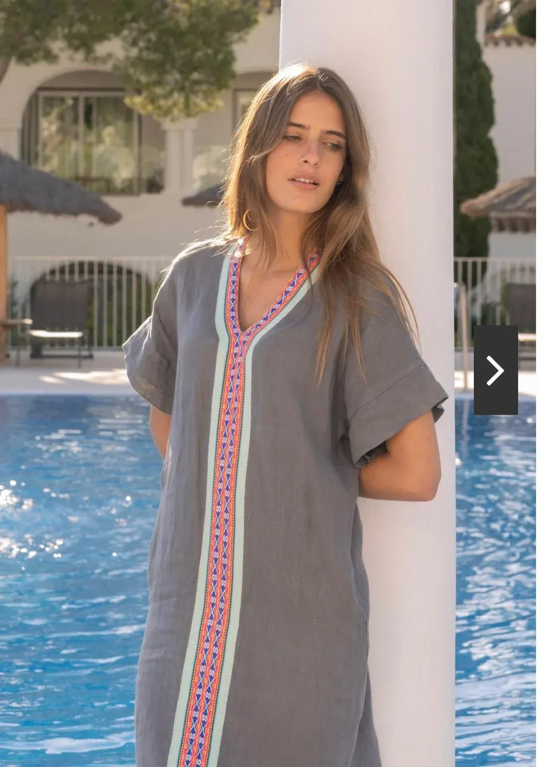 Una mujer con un vestido gris y ribetes coloridos se encuentra junto a una piscina.