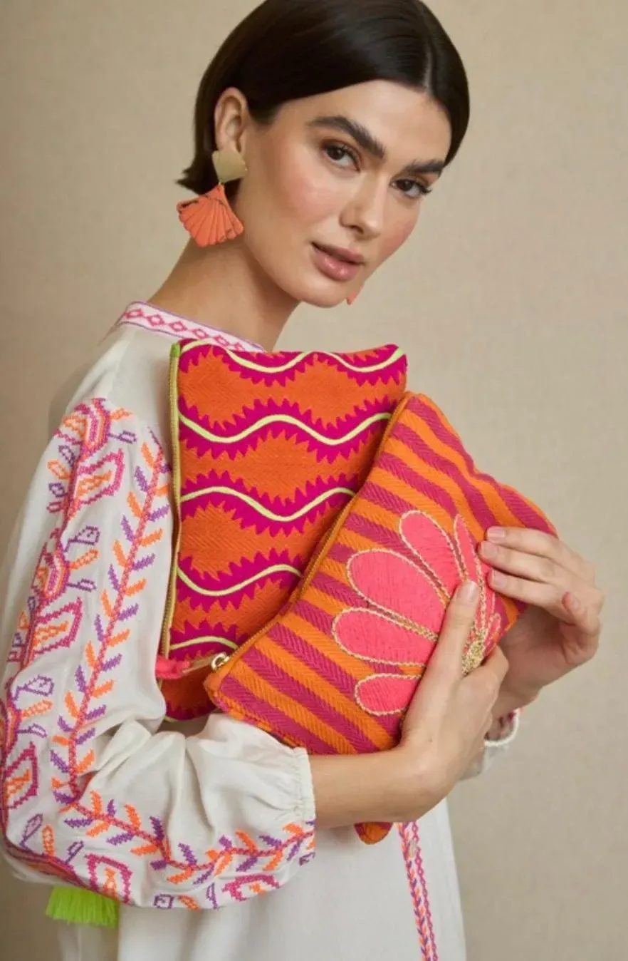 Mujer sosteniendo dos bolsos bordados de colores, vistiendo un vestido blanco bordado y pendientes con borlas.