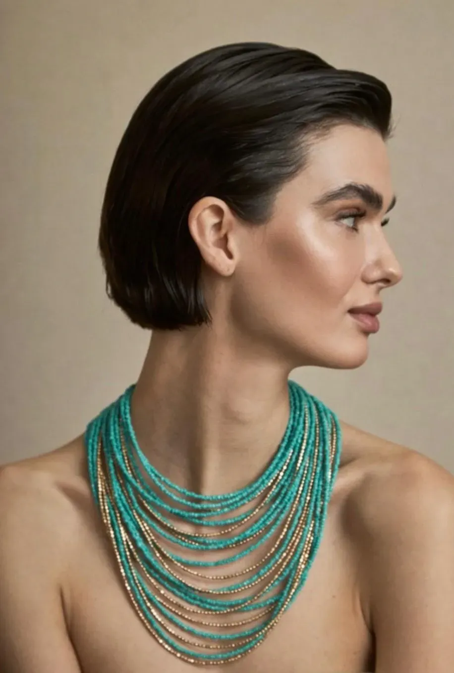 Mujer con collar de capas de turquesa y oro, cabello corto y oscuro, mirando hacia la derecha.