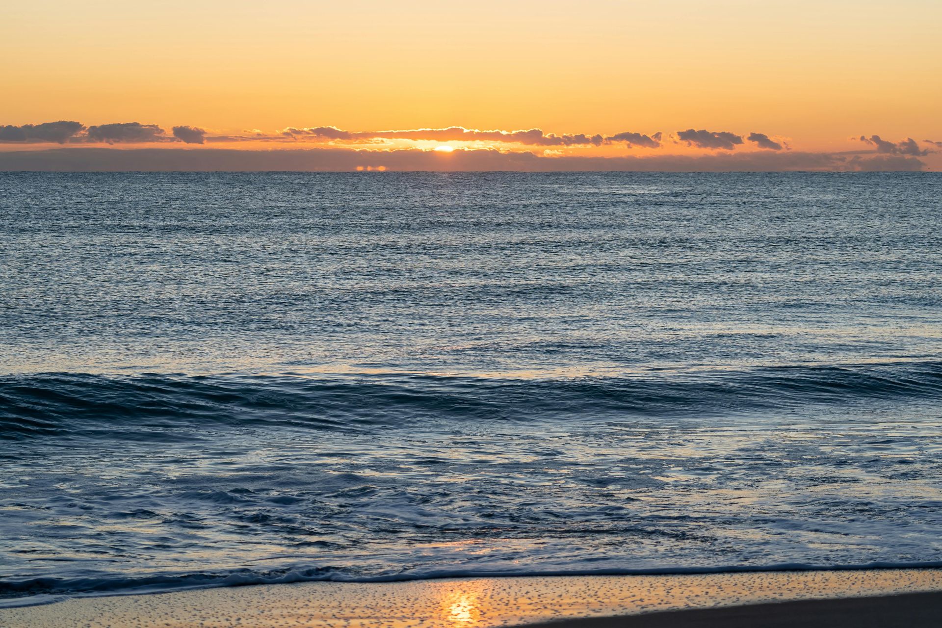 Olas del océano al amanecer con cielo naranja reflejándose en el agua.