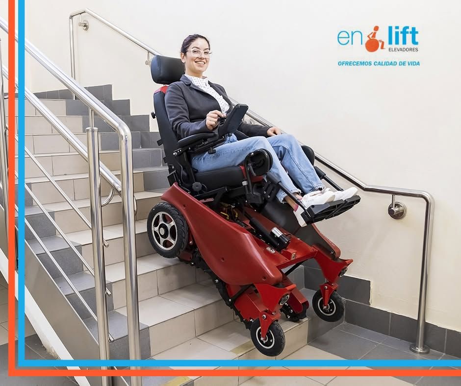 Mujer en silla de ruedas en una plataforma elevadora roja subiendo una escalera interior.