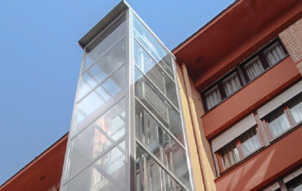 Torre de ascensor de cristal junto a un edificio rojo contra el cielo azul