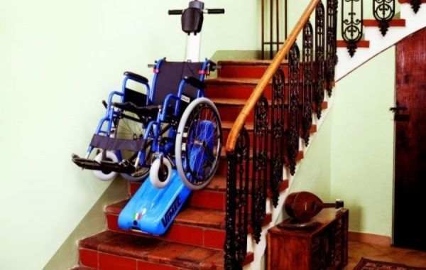 Silla de ruedas en una escalera con rampa azul, que pone de manifiesto la inaccesibilidad de la entrada a la vivienda.