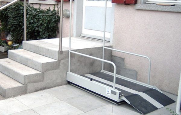 Rampa portátil para sillas de ruedas junto a las escaleras que conducen a la entrada de un edificio.