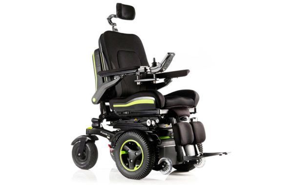 Silla de ruedas eléctrica negra con reposacabezas y controlador tipo joystick sobre un fondo blanco.