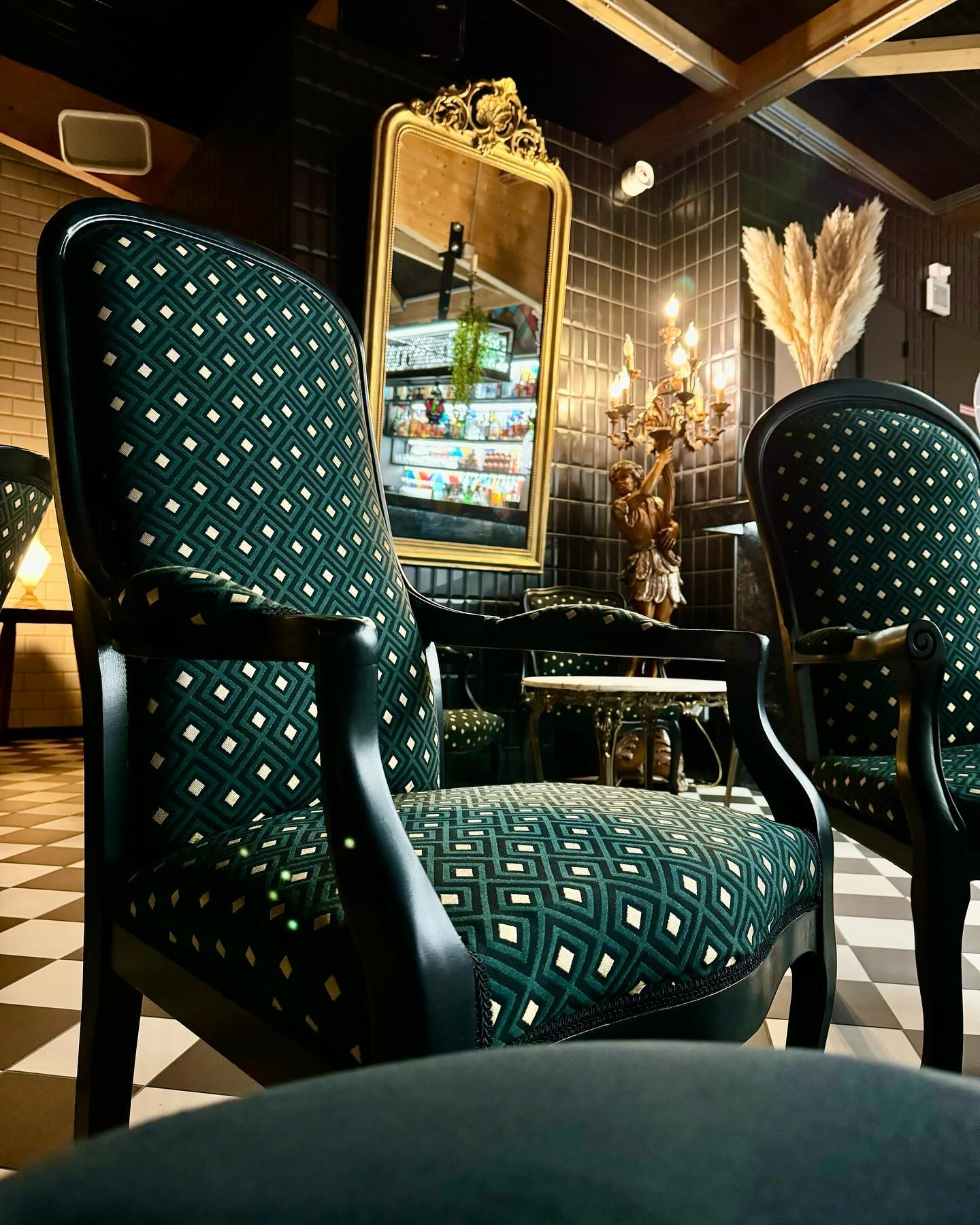 Salon élégant avec des fauteuils vert foncé à motifs, un miroir doré et un éclairage chaleureux