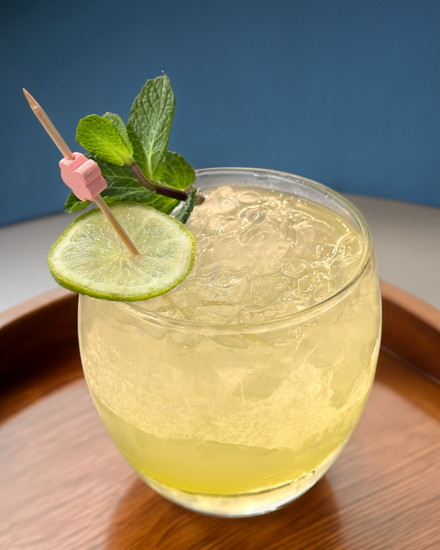 Un cocktail au citron vert avec de la menthe et des glaçons, servi dans un verre bas sur un plateau en bois.