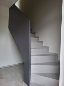 Una scala con gradini grigio chiaro e un'alta parete divisoria grigio scuro in una stanza moderna dai toni neutri.
