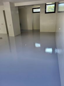 Una stanza pulita e vuota con pavimento in resina epossidica grigio chiaro lucida, pareti bianche e finestre rettangolari vicino al soffitto.
