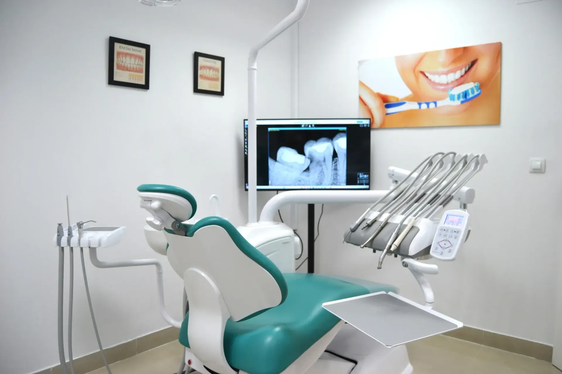 Sala de exploración dental con sillón para el paciente, monitor que muestra rayos X e instrumental dental.