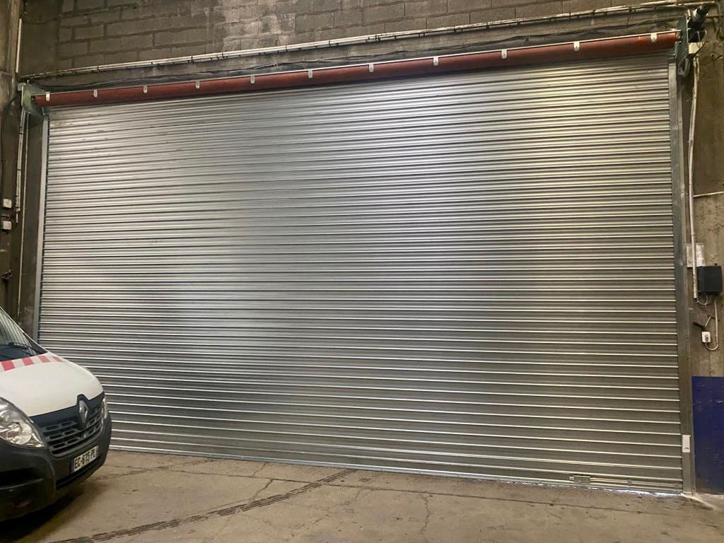 Porte de garage métallique argentée fermée, une voiture partiellement visible sur le bord gauche.