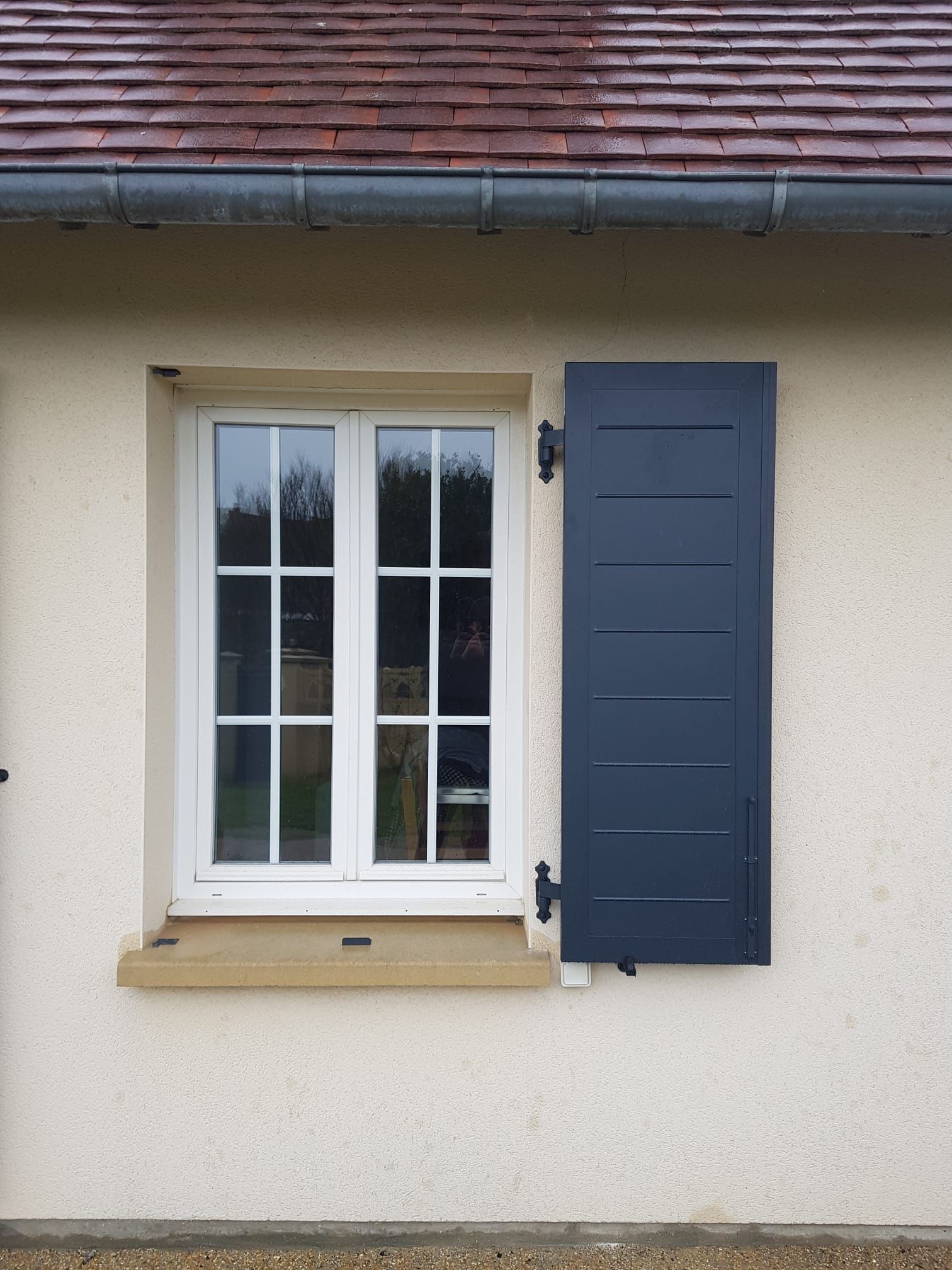 Fenêtre à cadre blanc avec volets bleu foncé sur un mur beige.