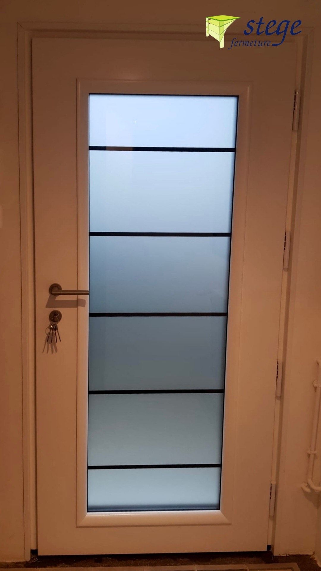 Porte blanche avec panneaux de verre dépoli et poignée en métal dans un couloir beige.