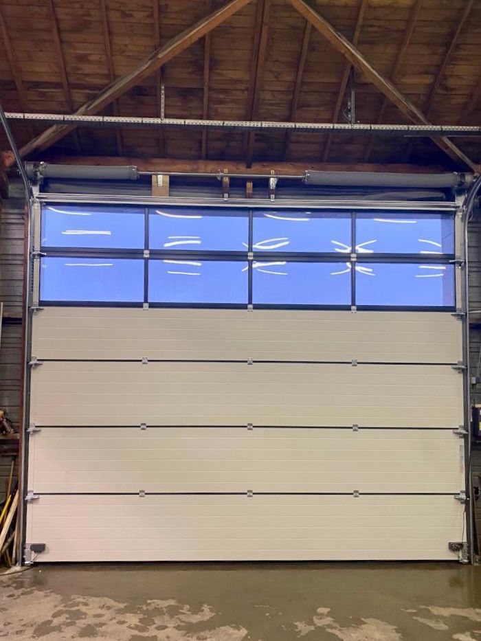 Porte de garage beige fermée à l'intérieur d'un entrepôt, avec des fenêtres teintées bleutées en partie supérieure.