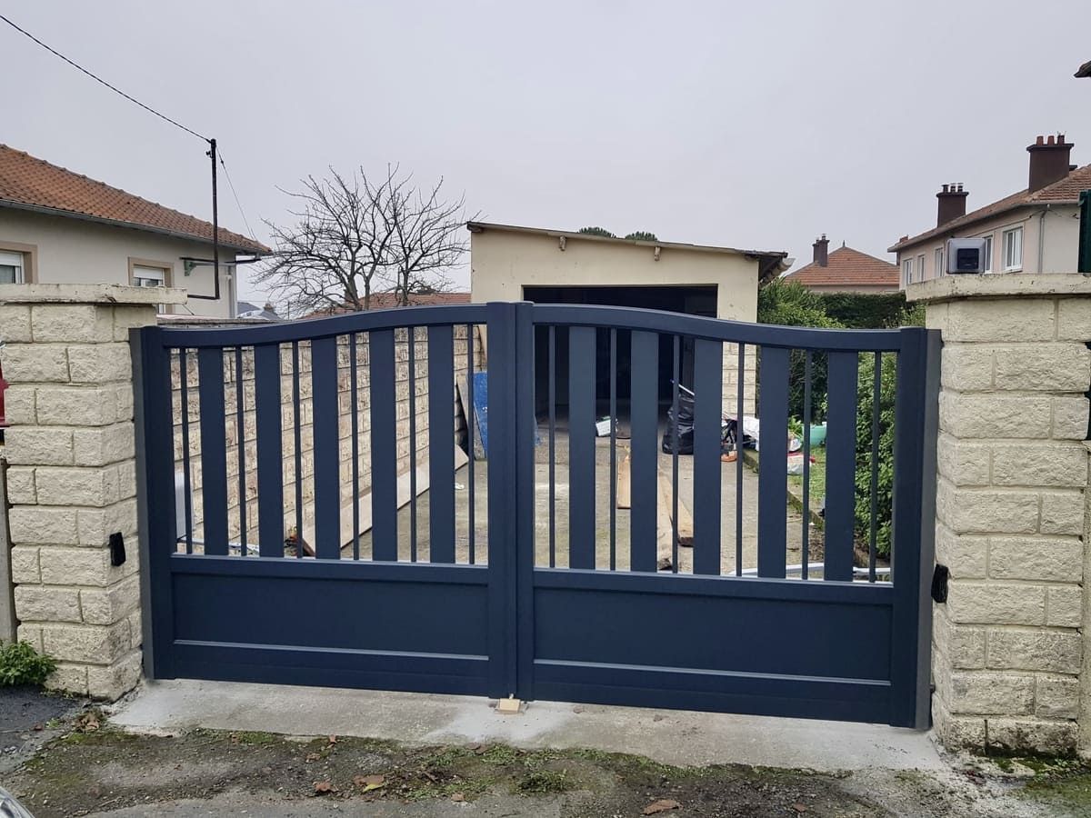 Portail d'allée en métal bleu entre des piliers en pierre dans un quartier résidentiel