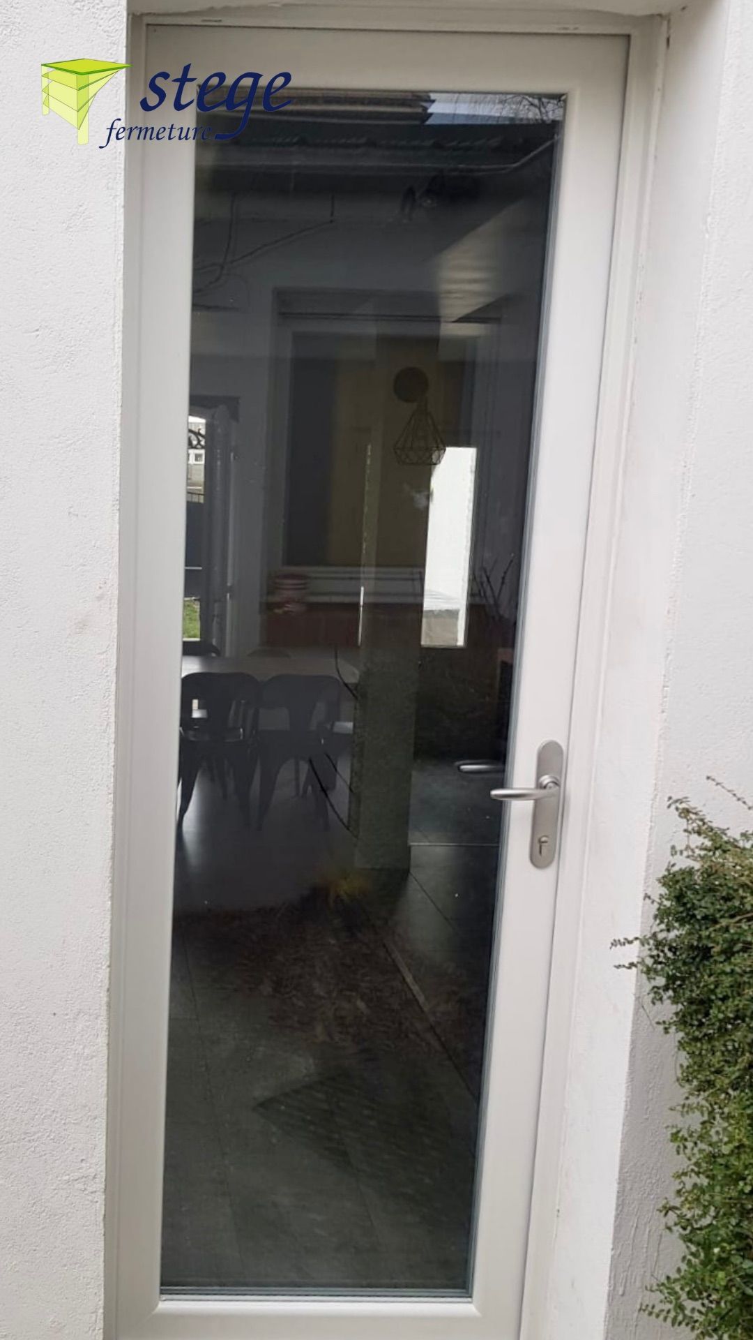 Porte extérieure blanche avec un haut panneau de verre et une poignée argentée, reflétant un couloir intérieur.