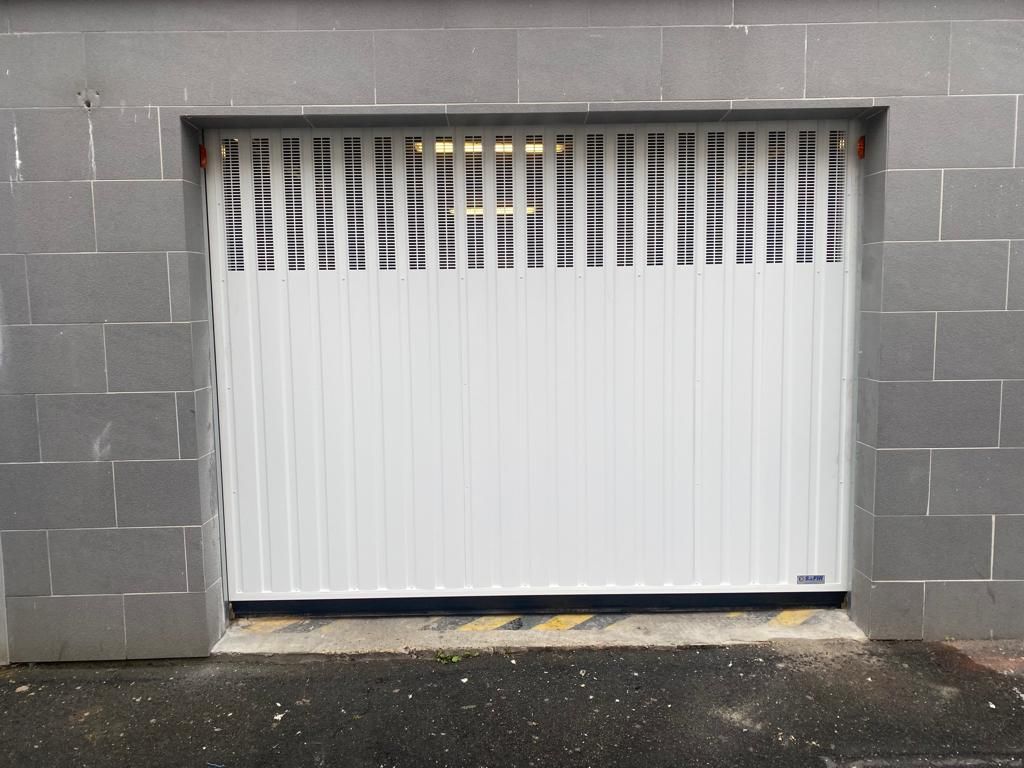 Porte de garage sectionnelle blanche encastrée dans un mur en parpaings gris