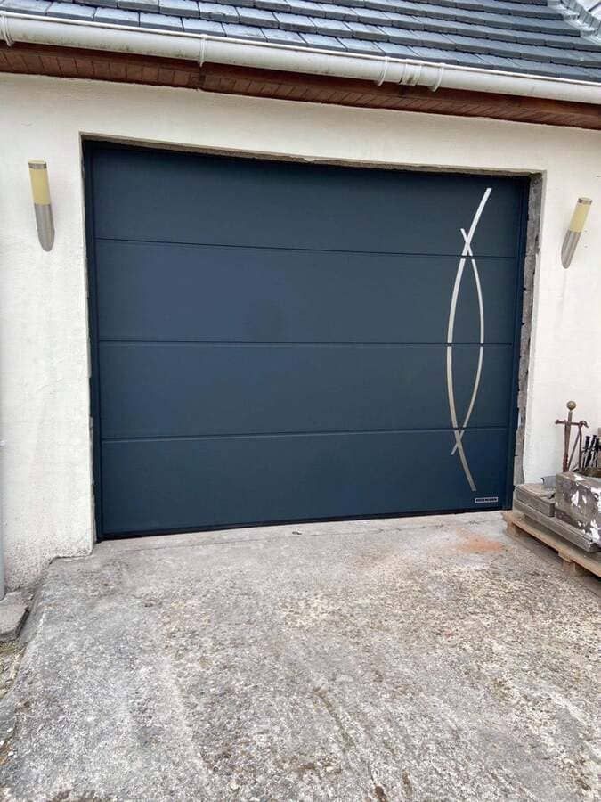 Porte de garage bleu foncé fermée avec encadrement blanc et allée en béton devant