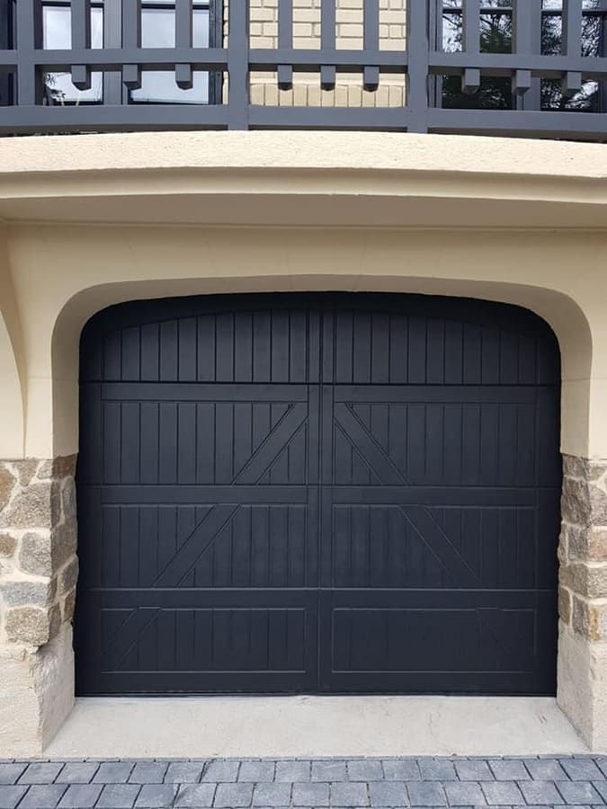 Porte de garage noire avec garniture en pierre cintrée sous un balcon.