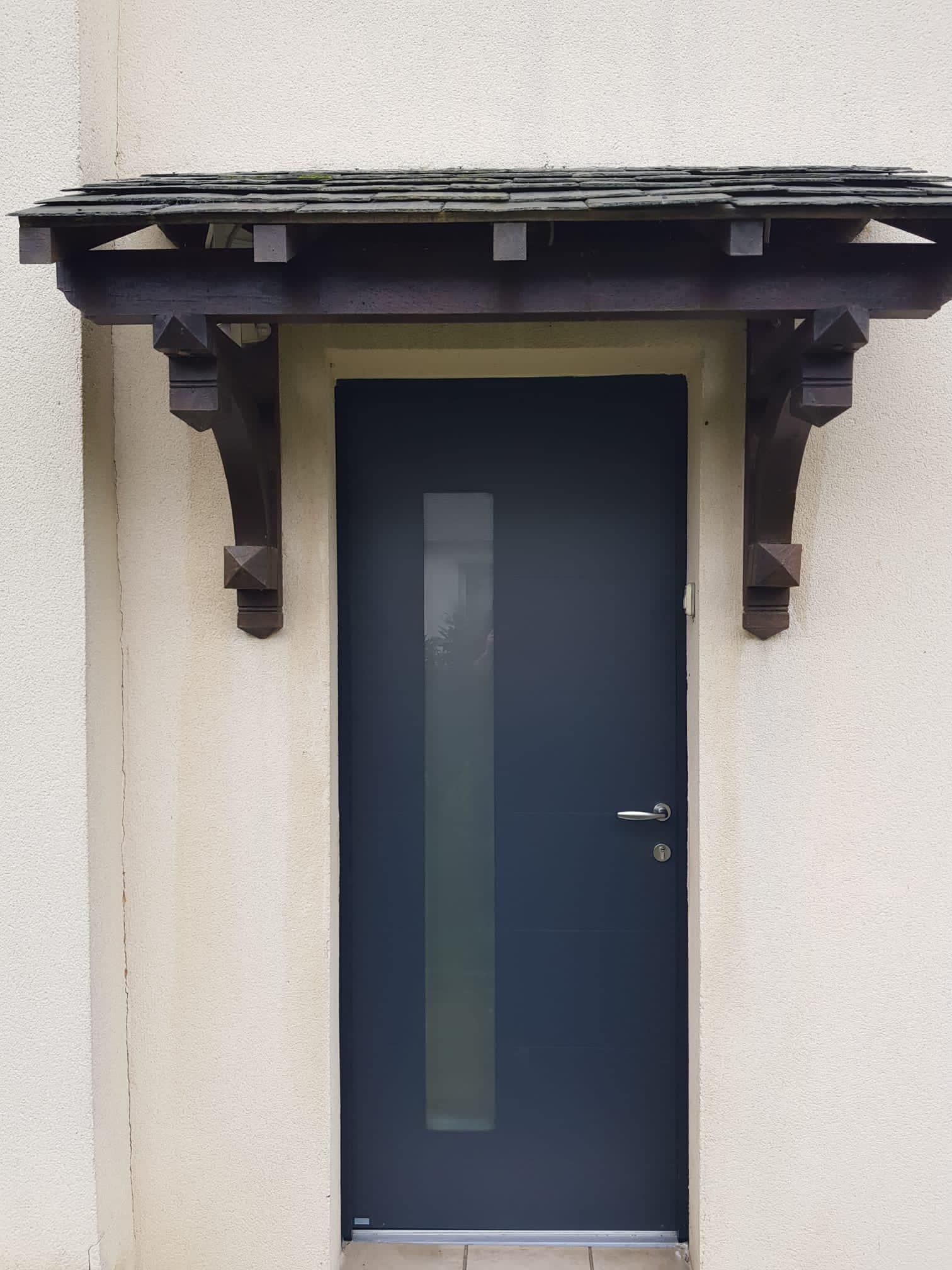 Porte d'entrée bleue sous un petit auvent en bois sur un mur beige