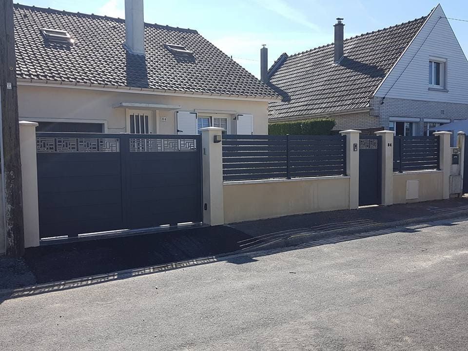 Maison de banlieue avec portail gris et clôture crème, située dans une rue résidentielle calme.