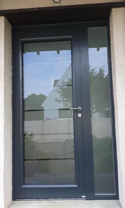 Porte d'entrée vitrée gris foncé avec panneau latéral dans un mur extérieur blanc