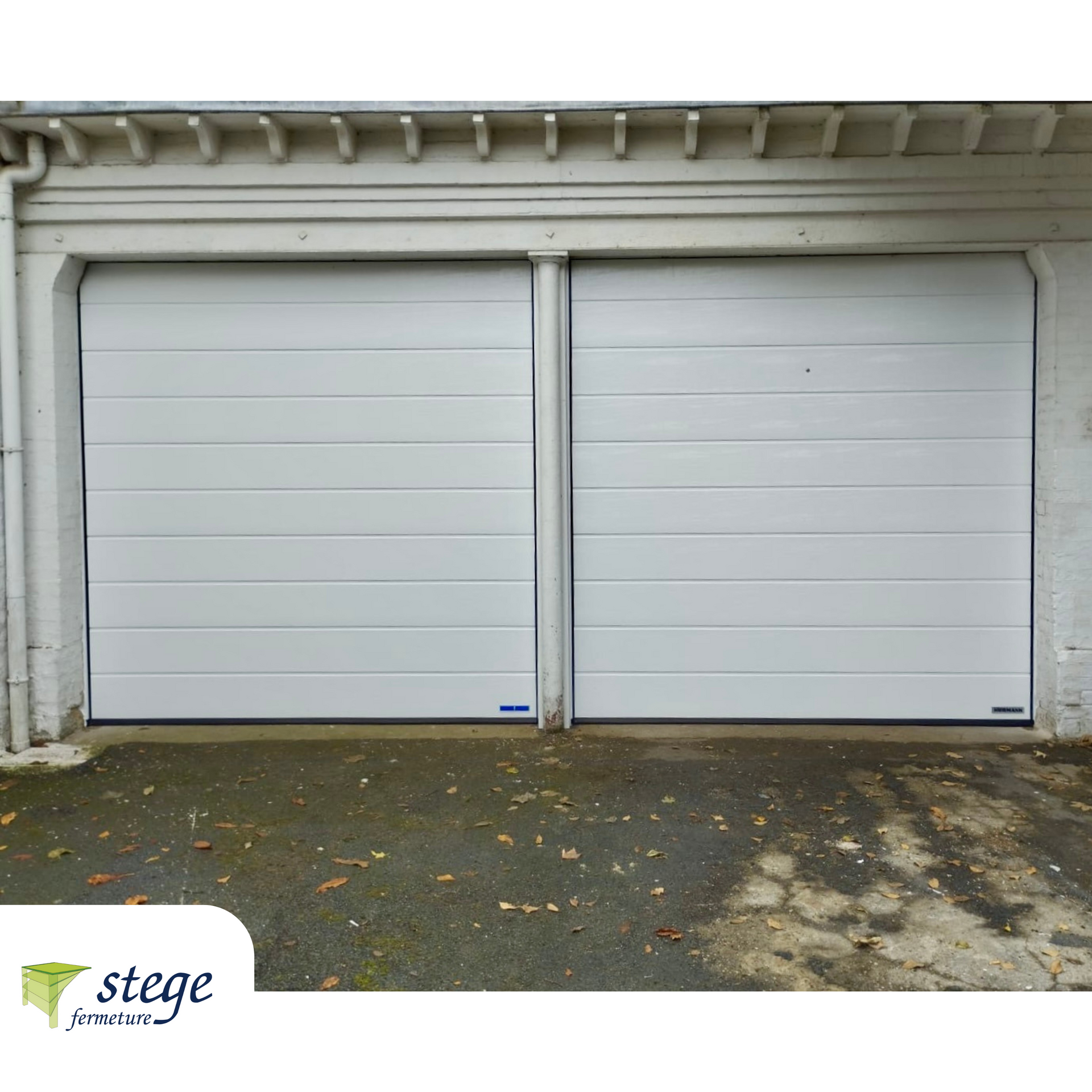 Deux portes de garage blanches sur un bâtiment à façade beige, avec un petit logo Stege en filigrane en bas à gauche.