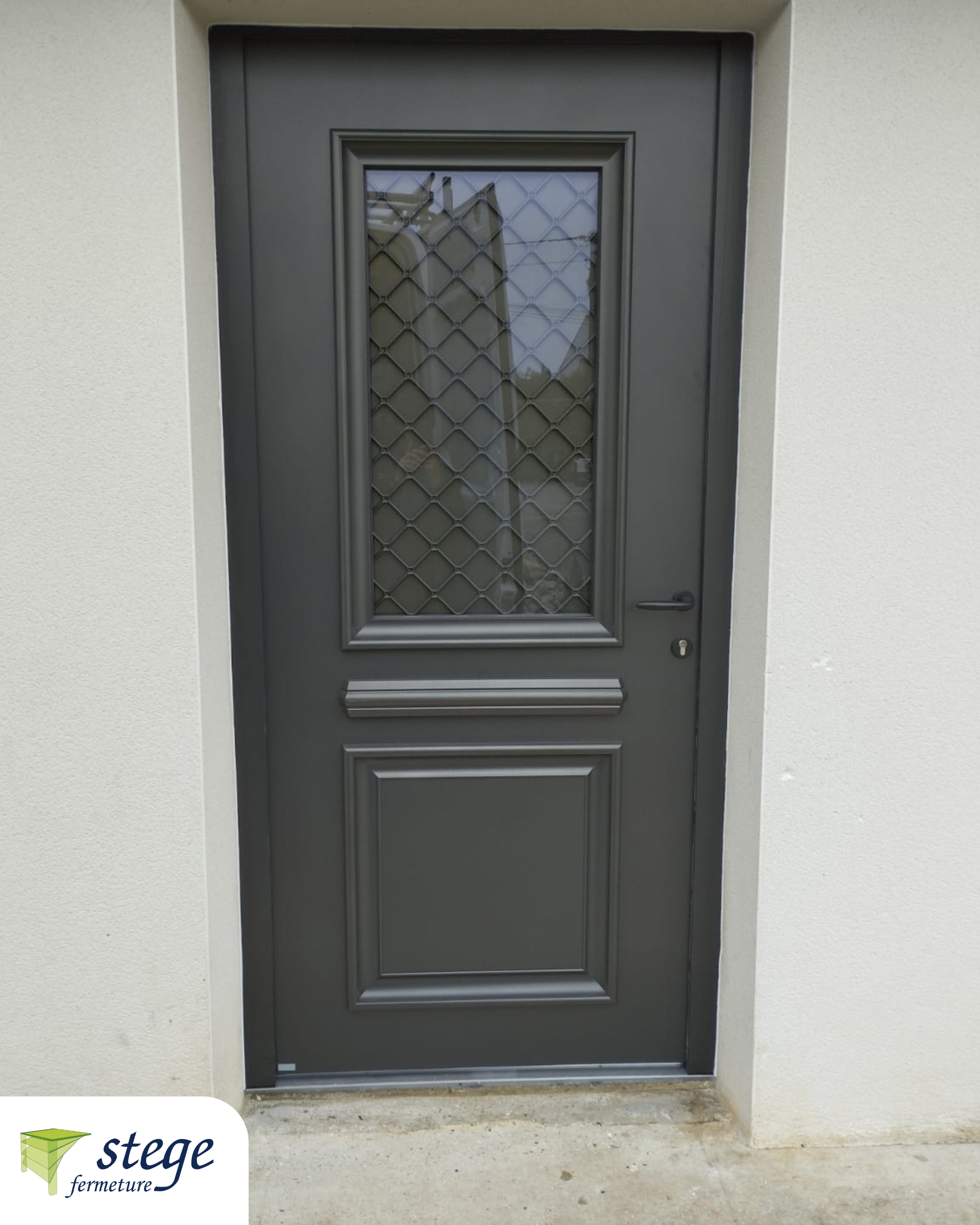 Porte d'entrée gris foncé avec une petite fenêtre et une grille de sécurité métallique encastrée dans un mur blanc.