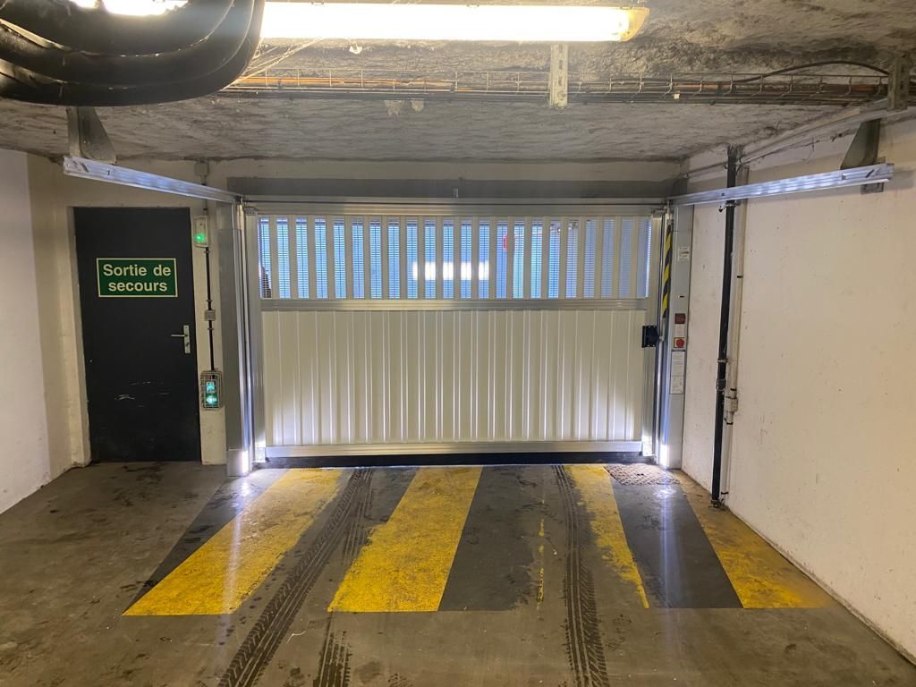 Entrée d'un parking intérieur avec marquages ​​au sol jaunes et portail métallique fermé.