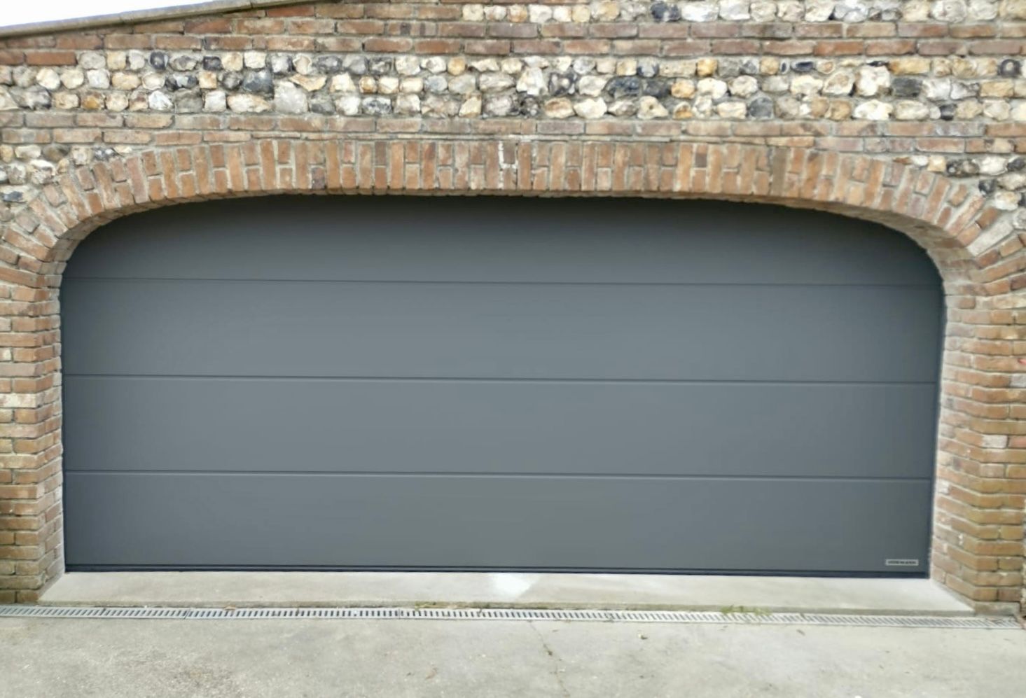 Porte de garage grise encastrée dans un mur voûté en pierre