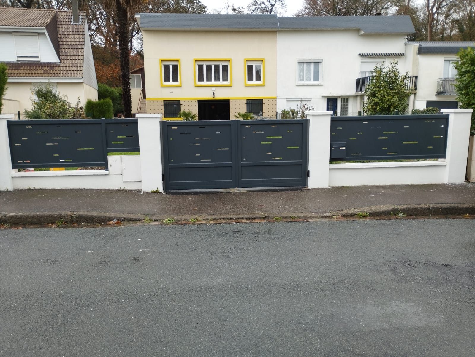 Rangée de maisons modernes avec des portails sombres et une façade jaune et blanche, dans une rue calme.