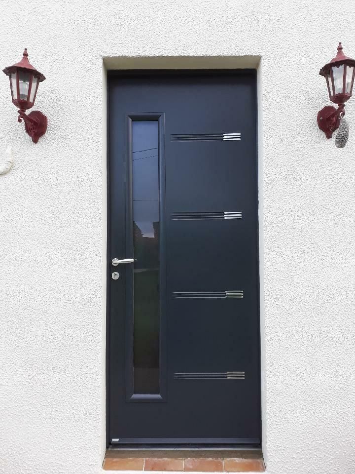 Porte d'entrée noire avec un étroit panneau de verre, flanquée de deux appliques murales sur une façade en stuc.