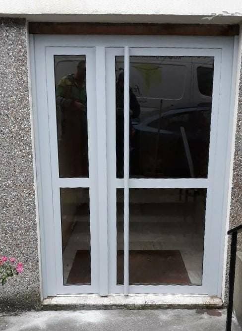 Porte double vitrée blanche avec panneaux latéraux verticaux dans un mur extérieur gris