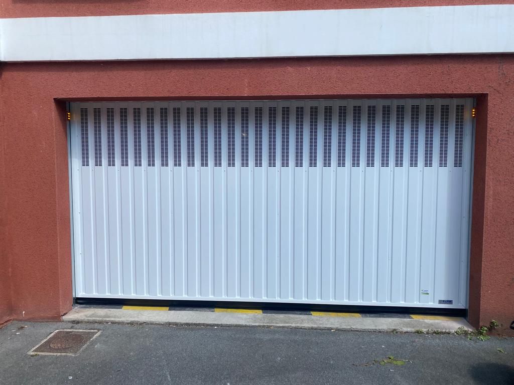 Porte de garage blanche dans un mur en stuc rouge avec un petit trottoir et une grille d'évacuation devant.