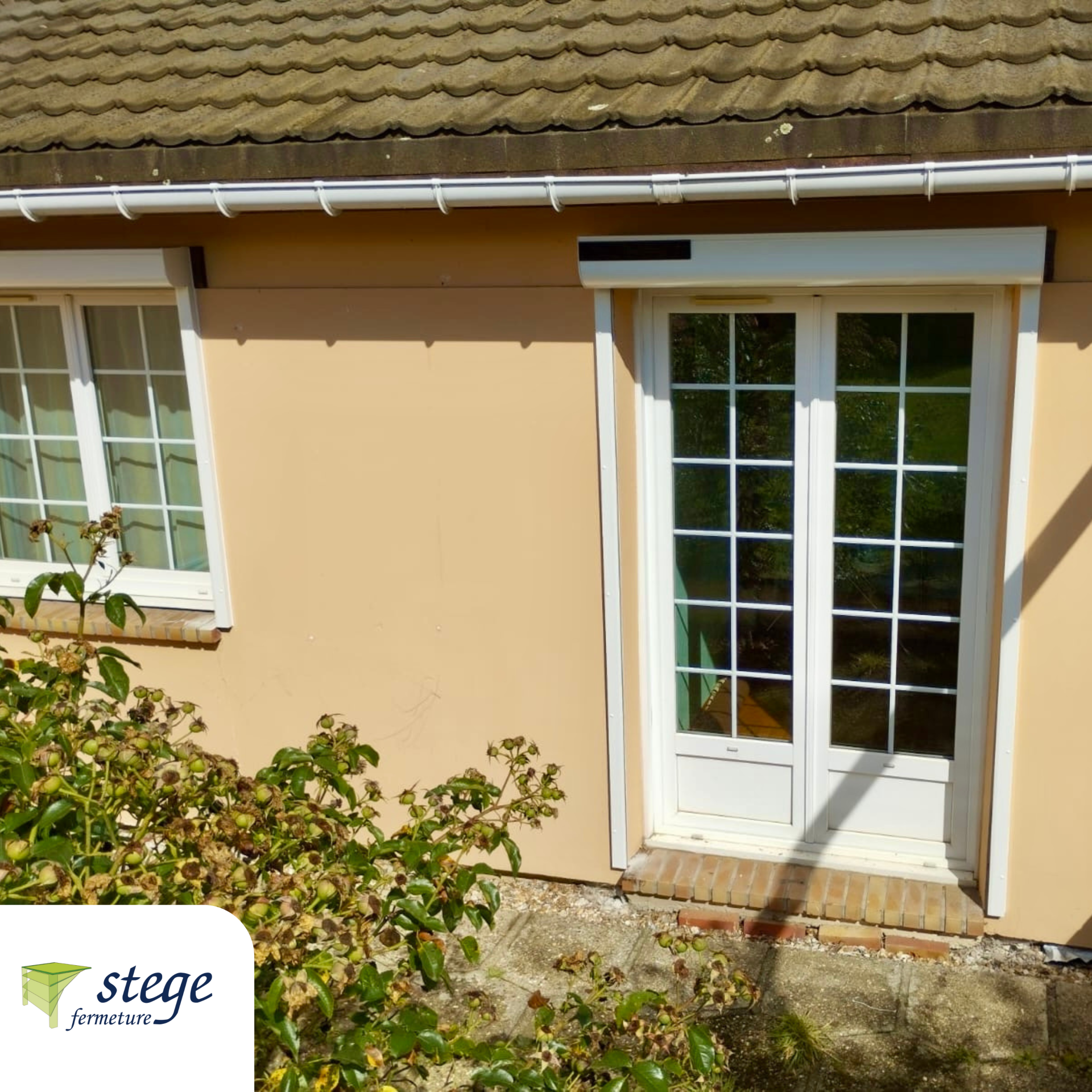 Maison beige avec porte-fenêtre et fenêtre blanches à côté d'un petit arbuste.