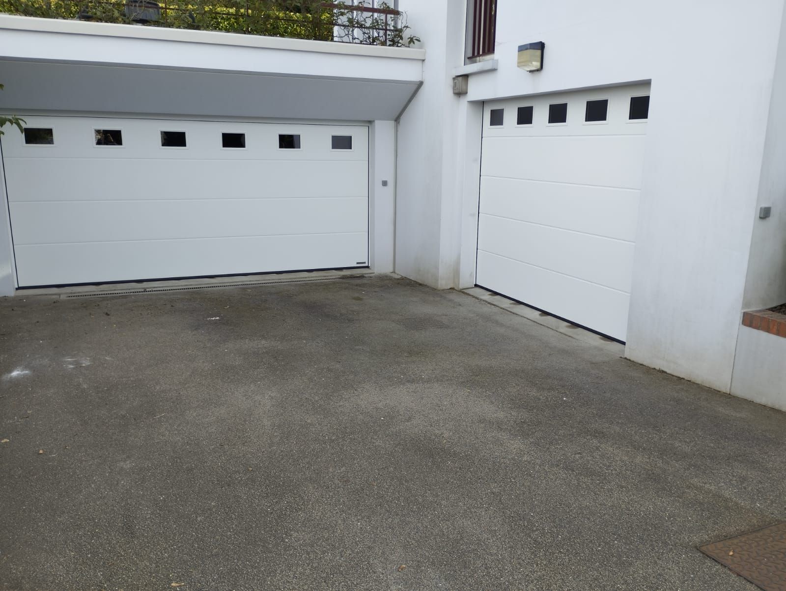 Deux portes de garage blanches sur une allée en béton à côté d'un bâtiment blanc