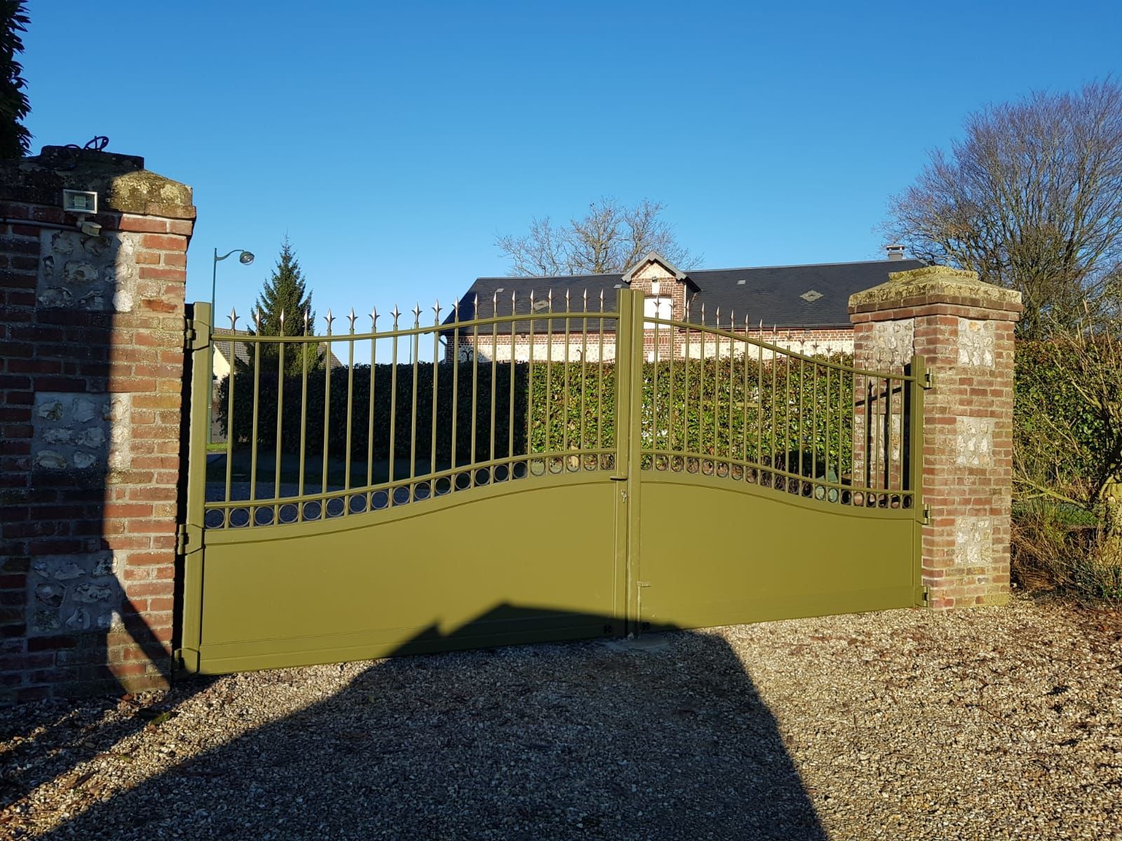 Portail métallique vert fermé entre des piliers de brique à l'entrée d'une allée de gravier