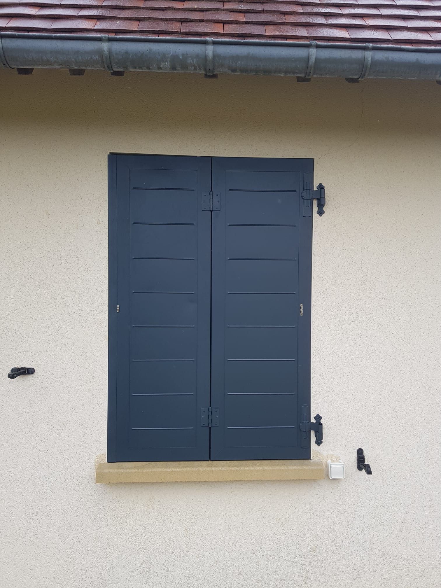 Fenêtre à volets bleu foncé sur un mur beige d'une maison, sous un avant-toit