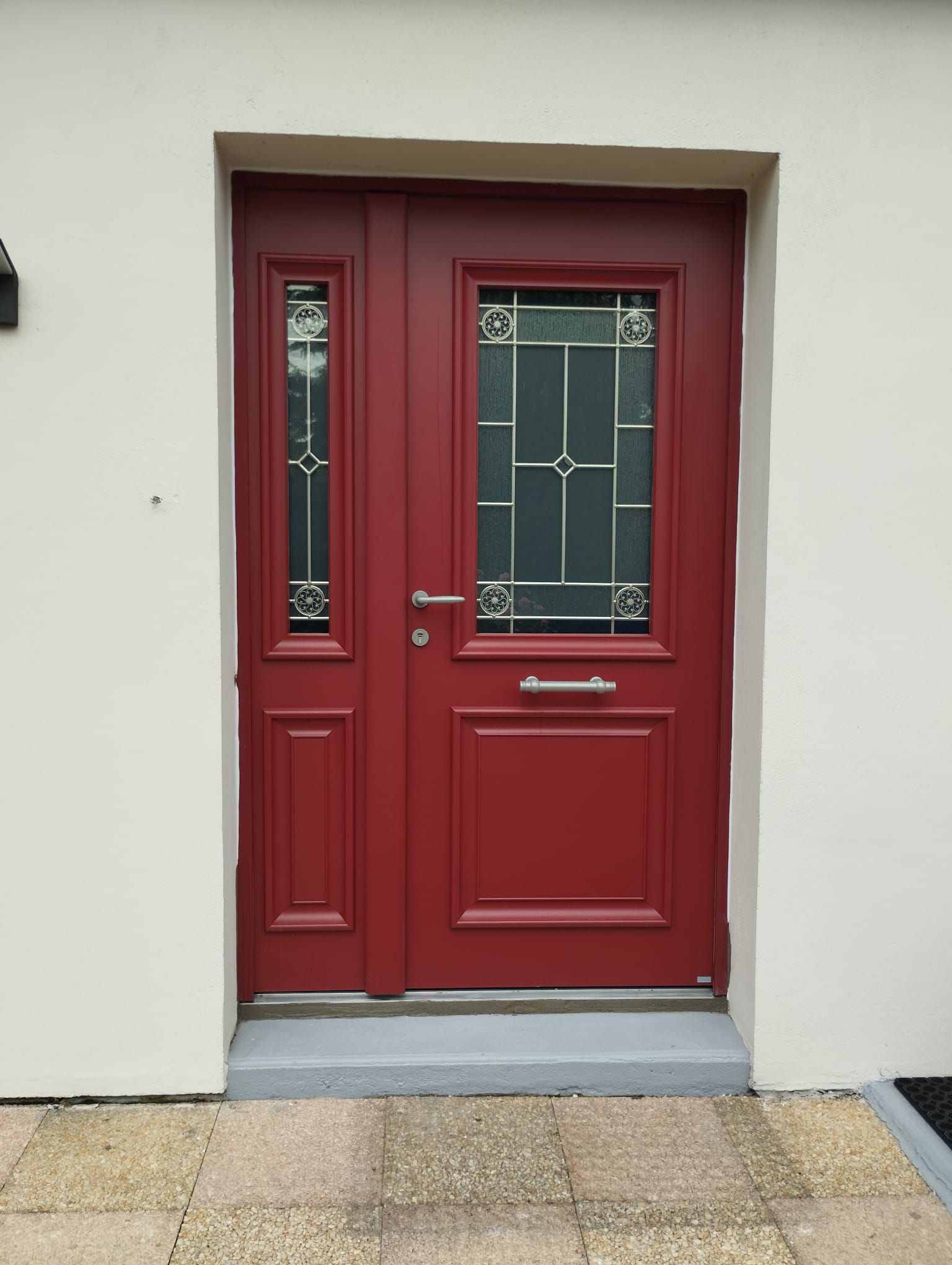 Porte d'entrée rouge avec panneaux de verre dans un mur extérieur blanc.