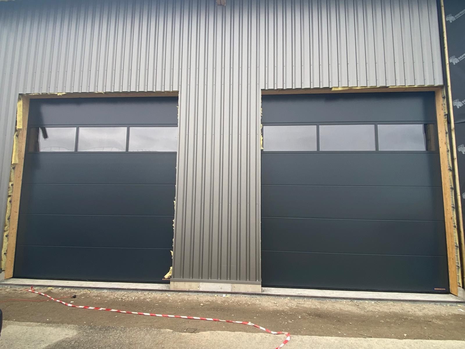 Façade de bâtiment industriel avec deux grandes portes de garage sombres et un mur en tôle ondulée
