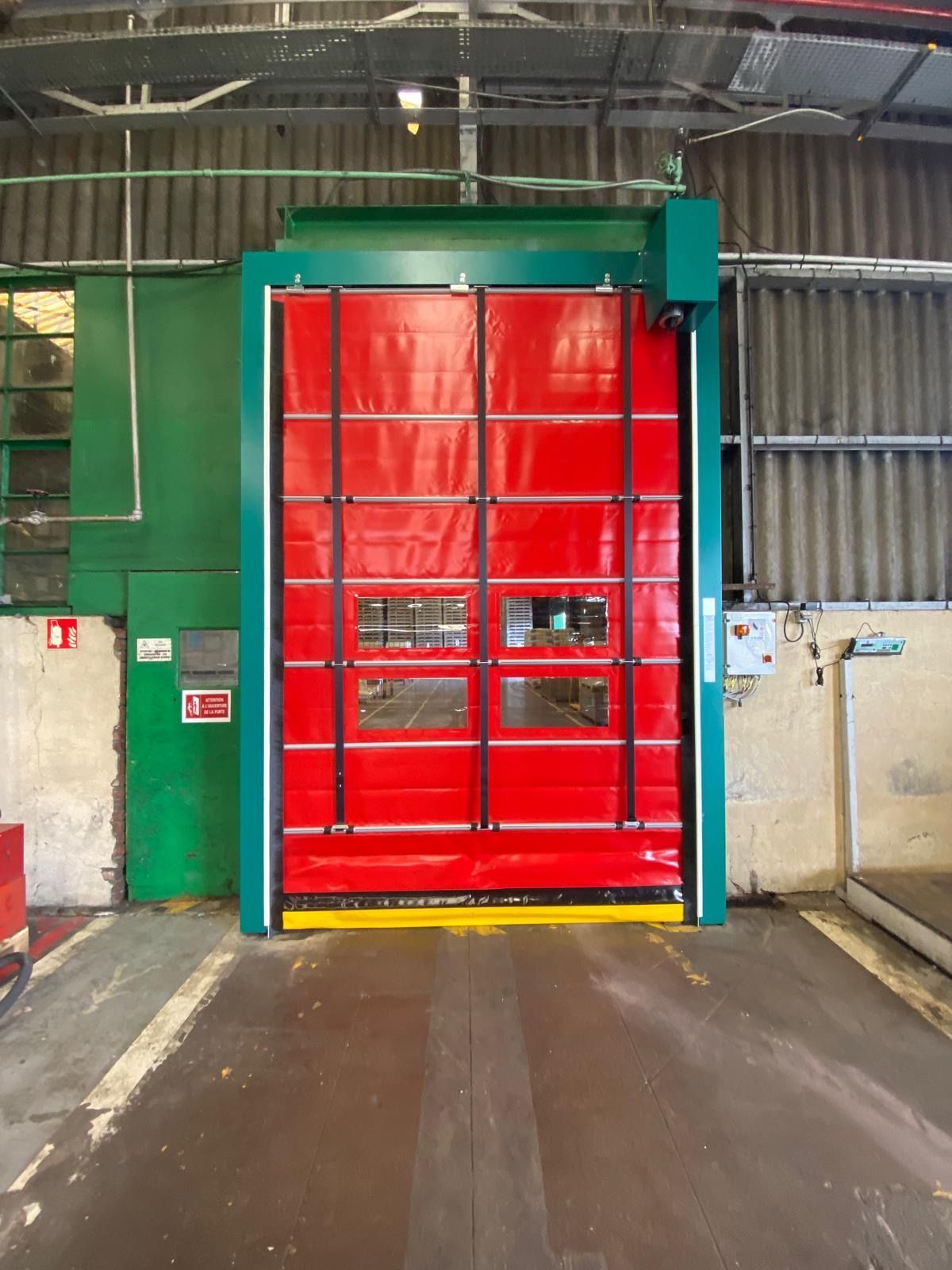 Porte de quai de chargement industrielle rouge avec cadre vert à l'intérieur d'un entrepôt.