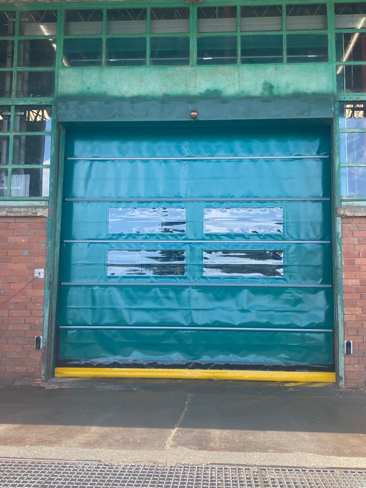 Porte sectionnelle industrielle verte avec petites fenêtres dans une façade de bâtiment en briques