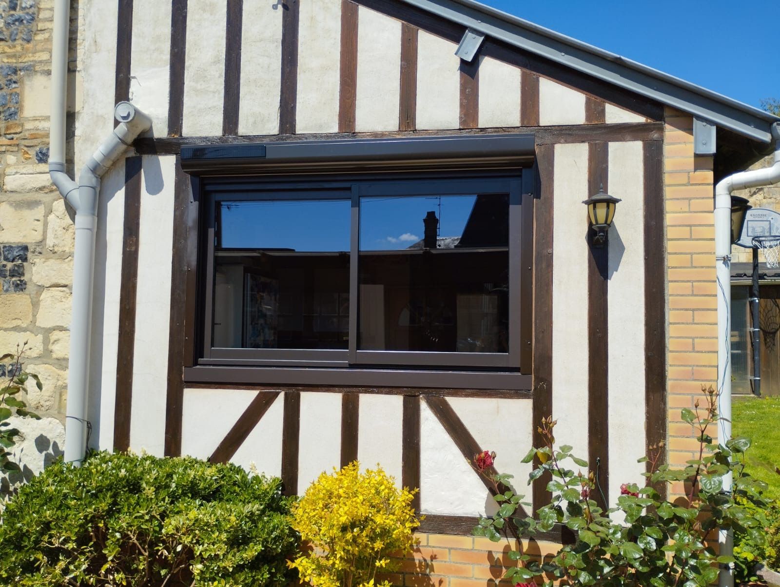 Façade d'une petite maison de style Tudor avec une fenêtre à cadre foncé et des murs blancs aux boiseries brunes.