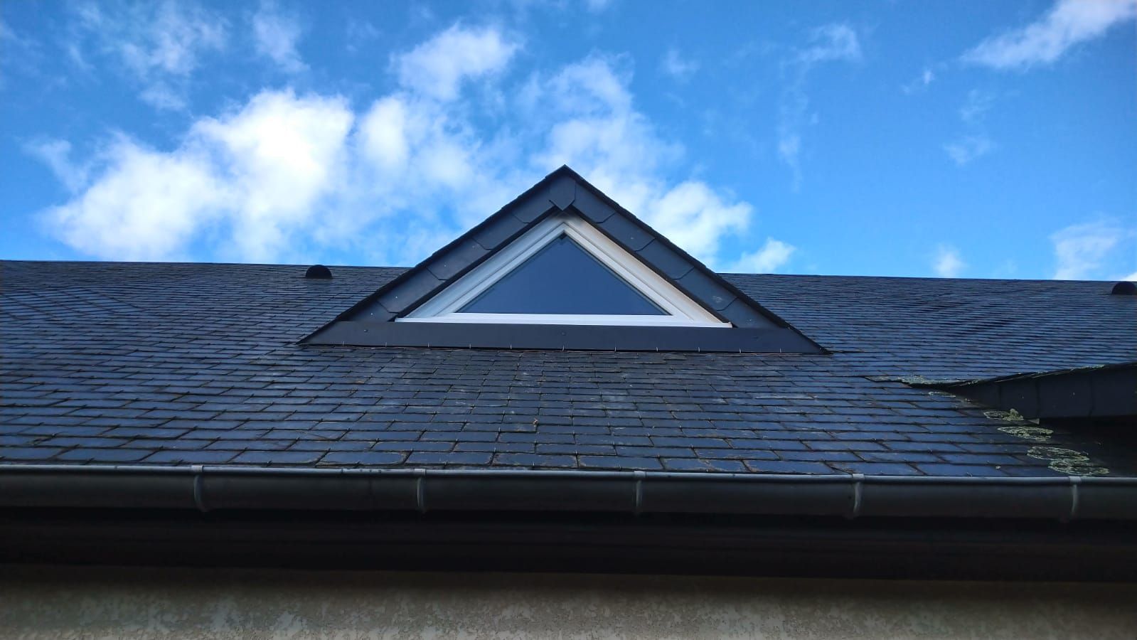 Toit avec une lucarne triangulaire sous un ciel bleu et des nuages