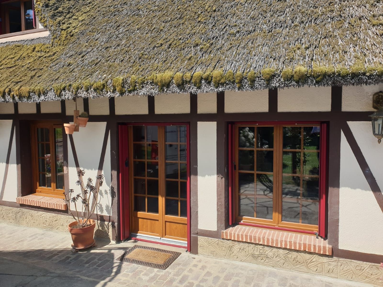 Façade de chaumière avec porte en bois, fenêtres à encadrement rouge et murs blancs