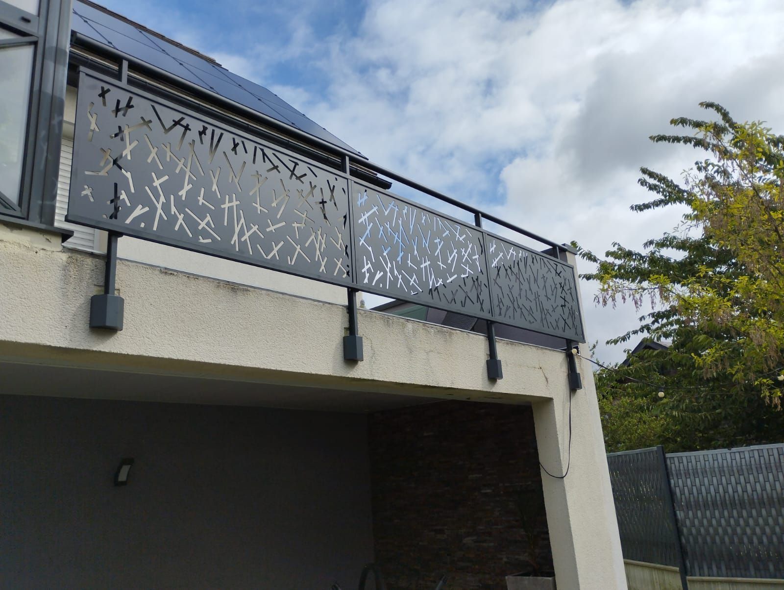 Balcon d'une maison moderne avec rambarde en métal à motifs sous un ciel nuageux