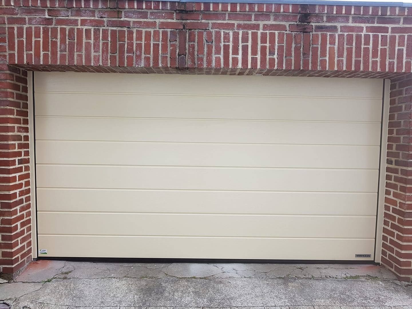 Porte de garage beige fermée encastrée dans un mur de briques rouges